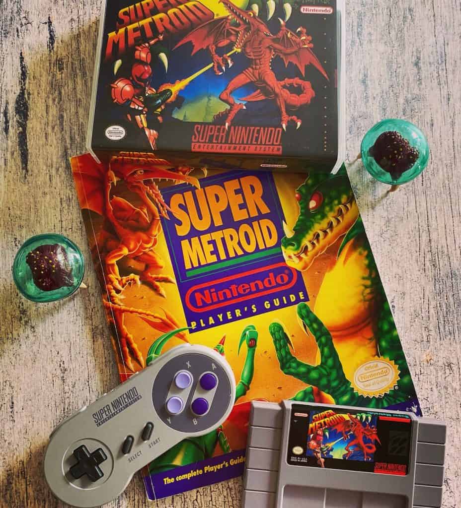 Super Metroid box, cart, Nintendo Power Player's Guide, SNES controller, and two Metroid figures